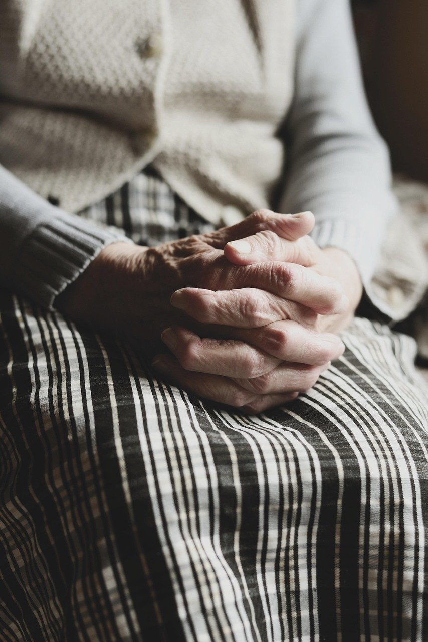 Femme âgée assise paisiblement les mains jointes, symbolisant la sérénité et le confort en fin de vie.