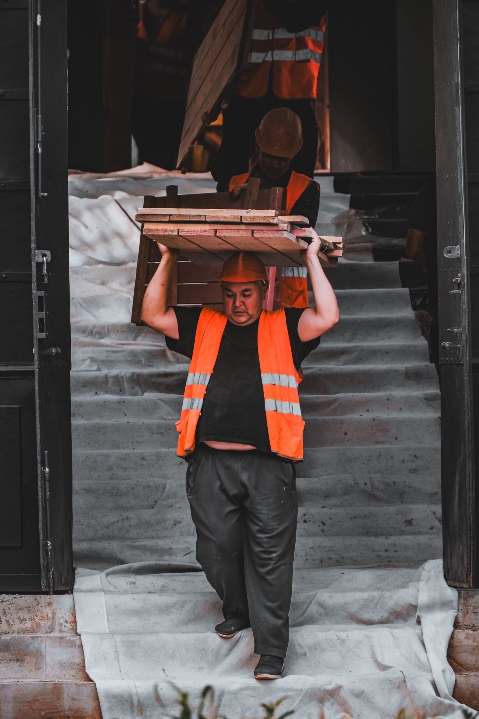 Ouvriers du BTP portant des charges lourdes sur un chantier, illustrant les risques de TMS.